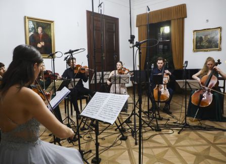 A photograph. A string concert in Villa Decius. The musicians play the violin and the cello in the Ball Room at Villa Decius.